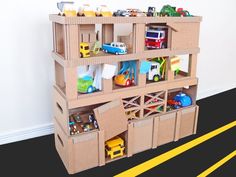 a cardboard toy storage unit with cars and trucks in it on the floor next to a yellow line