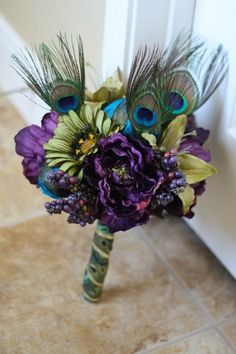 a bridal bouquet with peacock feathers and purple flowers on the floor next to a door