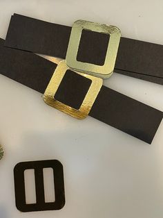 a pair of black and gold belts sitting on top of a white table next to a green plant