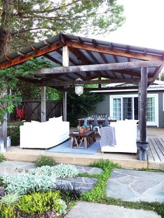 an outdoor living area with couches and tables under a wooden pergoline roof