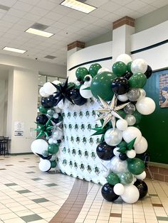 a balloon arch decorated with black, white and green balloons in the middle of a room