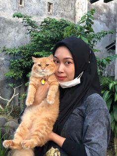 a woman in hijab holding a cat on her arm and looking at the camera