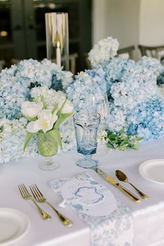 the table is set with blue and white flowers in vases, silverware, and napkins