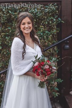 a woman in a white wedding dress holding a red bouquet and smiling at the camera