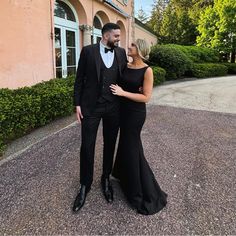 a man in a tuxedo and woman in a black dress posing for the camera