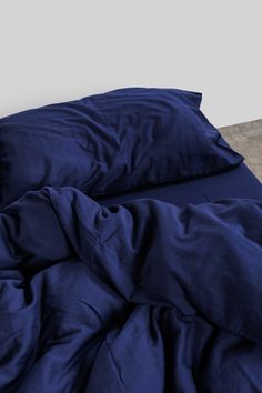 an unmade bed with dark blue sheets and pillow cases on top of the bed