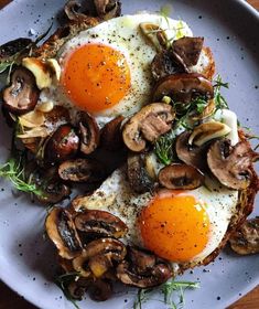 two fried eggs on toast with mushrooms and herbs in the middle, sitting on a white plate