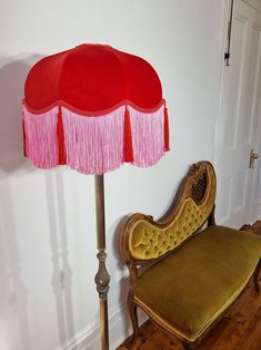 a red and pink lamp sitting on top of a wooden floor next to a chair