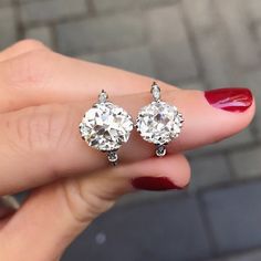 a woman's hand holding two diamond earrings