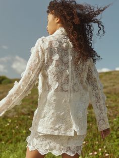 a woman is walking in the grass with her hair blowing in the wind while wearing a white lace dress