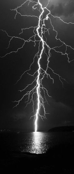 a lightning bolt is seen over the ocean in this dark night sky with water and clouds