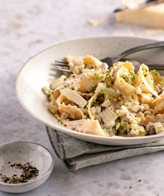 a white bowl filled with pasta and meat on top of a table next to a fork