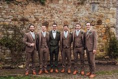 a group of men standing next to each other in front of a stone wall wearing suits and ties