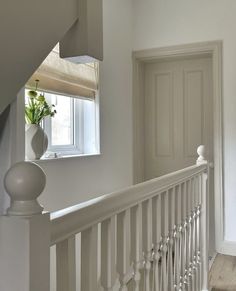 a white staircase with a vase on the bannister and a window in the background