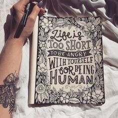 a person holding a pen and writing on top of a book with the words life is too short to be angry