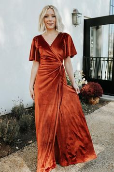 a woman wearing an orange velvet dress standing in front of a white building with her hands on her hips