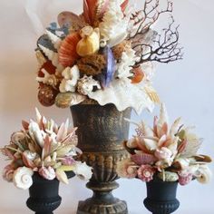 three vases filled with flowers and seashells on top of a white table