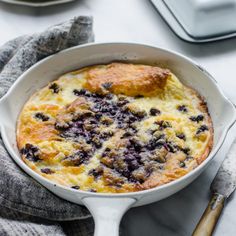 a blueberry cobble in a white dish on top of a table with silverware