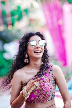 a woman in a pink and gold sari smiles while holding her hands out to the side