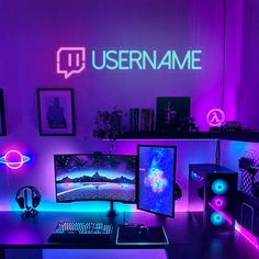 a computer desk topped with two monitors next to a purple neon sign and other items