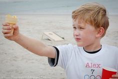 a young boy holding up a cup and ice cream cone on the beach with an olympic sign in the background