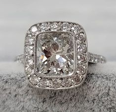 an engagement ring with a cushion cut diamond surrounded by pave diamonds on a furry surface