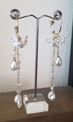 White Flower Dangle Drop Earrings Measuring a little over 4 inches long, these beautiful earrings feature lustrous high-quality acrylic flowers accented with beautiful faux pearl and crystal. Perfect for Bridal and Wedding wear, Anniversary, Easter, high tea, and Brunch! Details: High-Grade Acrylic Floral Motifs Crystal Faux Pearl 4 inches in Length Selectively Procured Stock item Ships in 1-3 days Delicate White Crystal Earrings For Party, White Pearl Charm Chandelier Earrings For Party, White Clip-on Bridal Earrings For Party, Elegant White Flower Earrings With Pearl Charm, White Pearl Drop Crystal Earrings For Evening, Pearl White Dangle Pearl Flower Earrings, Pearl White Dangle Flower Earrings, Pearl White Pearl Dangle Flower Earrings, White Crystal Clip-on Earrings For Party