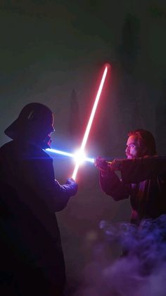 two people with lightsabens in the dark, one is holding a light saber