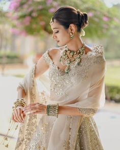 a woman in a white and gold outfit with jewelry on her neck, standing outside