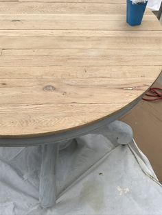 a round wooden table sitting on top of a sheet of paper next to a blue cup