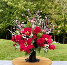 a vase filled with red flowers sitting on top of a wooden table next to trees