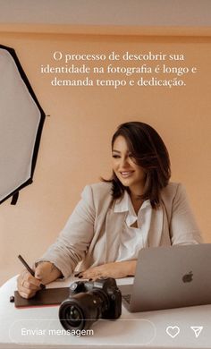 a woman sitting at a desk with a laptop computer and camera in front of her