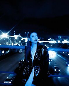 a woman with blue makeup is sitting on a ledge in the middle of a city at night