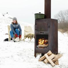 a woman sitting in front of an open fire pit on top of snow covered ground