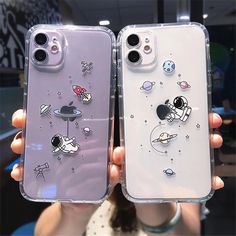 two people holding up their cell phones with space themed cases on them, one is purple and the other is white