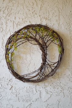 a twig wreath hanging on the side of a white stucco wall with green leaves