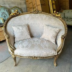 an ornate chair with two pillows on it in front of a mirror and other antique furniture