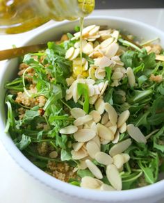 a white bowl filled with greens and almonds being drizzled with olive oil