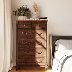 a bedroom scene with focus on the chest of drawers and white bed linens in the foreground