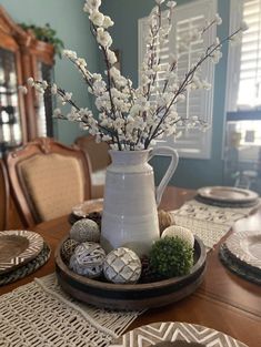 a white pitcher filled with flowers sitting on top of a wooden table next to plates