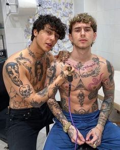 two men with tattoos on their bodies sitting next to each other