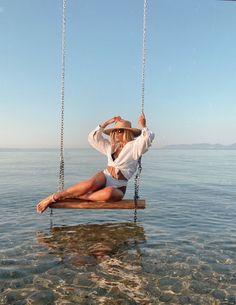 a woman is sitting on a swing in the middle of the water while wearing a hat and sunglasses