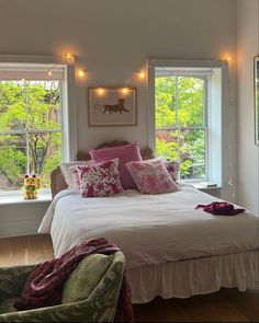 a white bed sitting in a bedroom next to two windows with fairy lights on them