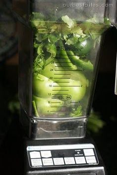 a blender filled with green vegetables sitting on top of a black counter next to a measuring cup