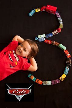 a young boy laying on top of a table next to a toy car track with cars coming out of it