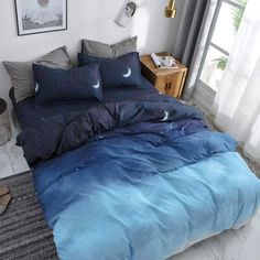 a bed with blue comforter and pillows in a white room next to a window