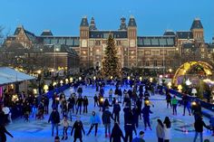 many people skating on an ice rink in front of a large building with christmas lights