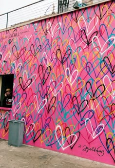 a pink wall with lots of hearts painted on it and a man looking out the window