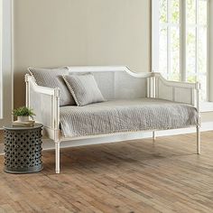 a white day bed sitting on top of a hard wood floor next to a window