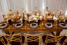 a wooden table topped with black and white plates next to tall vases filled with flowers